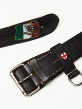 This collection includes two unique black leather belts, each adorned with metal buckles. One belt features an Italian flag and crest patch, while the other has a red cross on a white shield. Crafted by Blue de Gênes, both Gari Belts - Black embody premium leather accessories on a plain white surface.