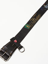 Introducing the Gari Belt - Black by Blue de Gênes: a distinctive leather accessory with a black strap, metal buckles, gold lettering, colorful designs, a red and white emblem, green patch, and celestial imagery for a historical or commemorative touch.