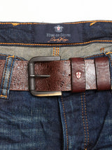 Close-up of blue denim jeans with orange stitching, paired with a Piceno Leather Belt - Cognac featuring a textured pattern and embossed logo. The inner label on these vintage-look jeans reads Blue de Gênes.