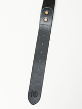 A close-up of the Piceno Leather Belt - Black by Blue de Gênes against a white background features a vintage look with two metal rivets, multiple holes along its length, and an embossed logo near the tip.