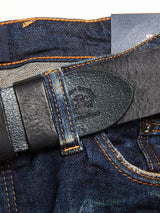 A close-up of dark blue denim jeans with orange stitching, partly concealed by the Piceno Leather Belt - Black from Blue de Gênes, creating a vintage look.