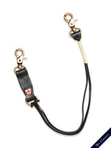 The BGsavino Key Hanger - Black by Blue de Gênes is shown on a white background, featuring black leather, stitched white detail, brass hardware at both ends, and a small red and white shield emblem.