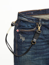 A close-up of blue denim jeans by Blue de Gênes shows visible wear, an England flag pin above the pocket, and a BGsavino Key Hanger - Black attached to a belt loop. A Made in Italy tag is visible inside the waistband.