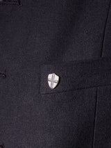 Close-up of the Black Casella Officers Blazer by Blue de Gênes, featuring a small silver shield-shaped pin with a cross, attached near a flap or pocket on the coarse texture typical of brushed cotton fabric reminiscent of vintage parade uniforms.