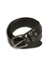 The Barra Belt by Blue de Gênes is a black cow leather belt featuring a silver buckle, a red and white shield emblem, vintage look, handmade stitches, several adjustment holes, and a rounded end.
