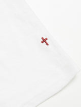 Close-up of the Lino T-shirt - White by Blue de Gênes featuring a small embroidered red cross near the raw edge on a light background.