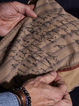 Hands cradle the Teo Chino - Antique Bronze cloth from Blue de Gênes, featuring script-like cursive on beige fabric with red stripes. The honeycomb weave is paired with a denim shirt and bracelets for a timeless look.