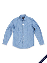 The Miguel Chambray Shirt in Lt. Denim Blue by Blue de Gênes is made from premium cotton, featuring a classic collar, long sleeves, and Corozo nut buttons. Its displayed on a white background with a small navy ribbon stating The Classics.