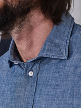 Close-up of a person in the Miguel Chambray Shirt - Lt. Denim Blue by Blue de Gênes, showcasing corozo nut buttons and textured cotton fabric, focusing on the collar and shoulder area with part of their beard and hair visible.