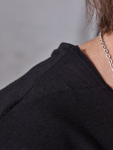 Close-up of a person wearing the Sagi Nuovo T-shirt - Black by Blue de Gênes and a silver chain necklace. The focus on the shoulder highlights the premium cotton texture and stitching, with a blurred background emphasizing this wardrobe staples beauty.