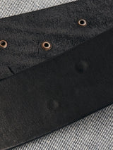 A close-up of the Blue de Gênes Cintura Belt in black shows metallic eyelets on a textured gray and white striped surface, boasting a smooth finish on one side, a slightly rougher texture on the other, and double buckle detailing with military inspiration.
