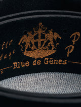 Close-up of the Cintura Belt - Black by Blue de Gênes. The vintage leather features a gold embossed logo and ornate crest with figures, elegantly resting on denim fabric in a classic, military-inspired design.