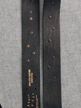 Close-up of two black leather belts on denim. Left belt looks vintage with gold text 100% Cow Leather Made in EU and multiple holes. Right belt has no visible text or holes. Both are Cintura Belt - Black by Blue de Gênes.