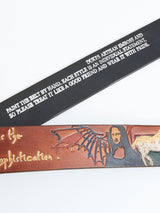 Two leather belts are displayed. The top black belt shows white embossed text on artisan craftsmanship. The bottom one is the Da Vinci Belt 4 cm - Brown by Blue de Gênes, featuring an intricate design with a Mona Lisa-like figure and a winged creature, epitomizing premium leather accessories.