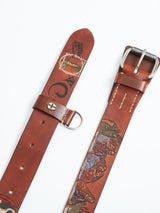 On a light background, two leather Blue de Gênes belts rest. The left one, the Da Vinci Belt 4 cm - Brown, features designs with text and illustrations inspired by Leonardo Da Vinci. The right belt mirrors these colorful illustrations along its length, both showcasing metal buckles and stitching details.