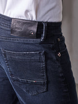 A person wears Vinci 3325 Black Jeans by Blue de Gênes, crafted with comfort stretch denim in Italy. The jeans feature a brown leather patch on the waistband, a visible back pocket, and button detail. A white shirt is partially tucked in.