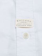 The Blue de Gênes BDGsandro Oxford Shirt in white features organic cotton fabric, a close-up of a button, and a small label that reads, "Buttons made of real natural corozo nut.