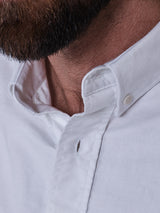 A close-up of the lower half of a person's face with a brown beard, wearing the Blue de Gênes BDGsandro Oxford Shirt in white with the top button undone.
