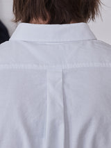 A close-up of a person wearing the Sandro Oxford Shirt - White from Blue de Gênes, crafted from organic cotton. The focus is on the back views upper half, showcasing the Sidogras seam and fabric texture. The persons hair is visible above the collar, adding to the sophisticated look.