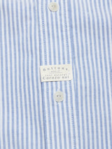 Close-up of the Sandro Oxford Shirt by Blue de Gênes features a blue-and-white vertical stripe fabric, buttons made from real corozo nuts, and a label noting organic cotton for sustainable style.