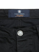 The Repi Stay Black Jeans from Blue de Gênes feature a close-up of black denim with an embossed metal button and a waistband blue label, showcasing style and flexibility with their slim-fit comfort stretch design.