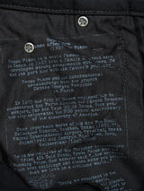 Close-up of text printed on black fabric with silver buttons, reminiscent of Repi Stay Black Jeans by Blue de Gênes. The text describes Renzo Piano, emphasizing his career and famous architectural works, while showcasing visible stitching and texture similar to comfort stretch denim.