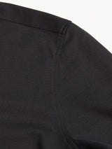 A close-up of the Luccio Dry Shirt in Jet Black by Blue de Gênes showcases the gently curved seam on its slightly textured cotton pique jersey fabric, suggesting a part of a garment.