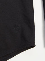 Close-up of the Luccio Dry Shirt - Jet Black by Blue de Gênes showcases a black textured fabric with a subtle circular pattern in the lower left, crafted from garment-dyed cotton pique jersey. The fabrics edge contrasts against a white background.