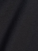 A close-up of the Luccio Dry Shirt in Jet Black by Blue de Gênes reveals its dark, textured cotton pique jersey with a subtle grid pattern. The garment-dyed surface appears slightly creased, casting gentle shadows and highlights across the fabric.