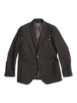 The Leopardi Carbonio Blazer by Blue de Gênes, made from Italian brushed cotton, features three buffalo horn buttons, two front pockets, and a subtle red lining. A small emblem adorns the left chest pocket of this black blazer.