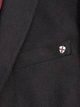 A close-up of the Leopardi Carbonio Blazer by Blue de Gênes highlights an elegant tailored pocket featuring a small shield-shaped pin with a red and white cross. Made from exquisite Italian brushed cotton, this black blazer embodies sophistication and style.