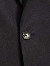 The Leopardi Carbonio Blazer - Black by Blue de Gênes, made from Italian brushed cotton, showcases a close-up of its black fabric with a single dark button. The button resembles buffalo horn, engraved with Blued Selected, and is secured through a well-stitched buttonhole.
