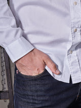 Wearing a Blue de Gênes Miguel Brilliante Shirt - White, crafted from fine Italian cotton and detailed with exquisite corozo nut buttons, a person stands with one hand in their pocket.