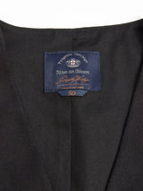 Close-up of a dark fabric garment labeled Blue de Gênes at the neck, displaying a shield and cross graphic with Produced in Italy and the number 50 in orange. Crafted from Italian brushed cotton, it features buffalo horn buttons. Product: Canna Carbonio Gillet - Black.