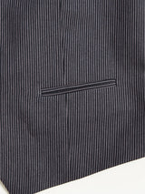 Close-up of a refined navy pinstriped suit pocket, reminiscent of the Canna Pallone Gillet by Blue de Gênes. Thin vertical white stripes adorn the fabric, enhancing its classic formal pattern, while the horizontal slit pocket seamlessly blends into the design.