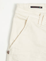 Close-up of Blue de Gênes Paulo Pavia 1 Chino in ecru, highlighting the pocket and waistband. A small Made in Italy flag label is attached at the top. Near the pocket seam, a shield-shaped logo highlights its cotton stretch fabric and soft texture.