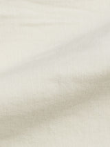 Close-up of the Paulo Pavia 1 Chino in ecru from Blue de Gênes, featuring off-white cotton stretch fabric with gentle folds and soft lighting that highlight its smooth texture. The subtle shadows evoke the depth seen in finely tailored chinos.