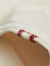 Close-up of Blue de Gênes Paulo Pavia 1 Chino in ecru, crafted from white cotton stretch fabric with eye-catching red stitching. The folded material reveals two parallel rows of red threads along the edge, contrasting against the plain background with a texture akin to smooth yet slightly wrinkled chinos.