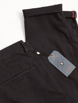 Two pairs of neatly folded Teo Chino - Jet Black pants by Blue de Gênes are displayed; one shows a back pocket and waistband. A navy blue tag with gold text highlights the garment dyed finish and brand details.