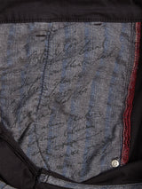 Close-up of the inside pocket of Blue de Gênes Teo Chino - Jet Black, showing gray and blue striped fabric with handwritten black ink, red stitching, a metal rivet, and partially faded text.