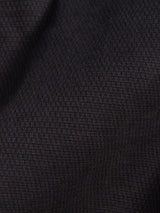 Close-up of Teo Chino - Jet Black by Blue de Gênes, showcasing dark honeycomb fabric with a subtle grid pattern and soft folds that create gentle shadows—an ideal material commonly used in chinos.