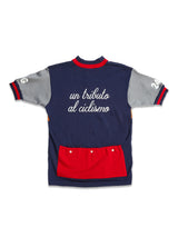The Tributo Cycling Jersey - Navy by Blue de Gênes is a vintage-style Merino wool outfit featuring navy, gray, and red. It has un tributo al ciclismo printed on the back, a red pocket, and white numbers 20 and 15 on the sleeves.