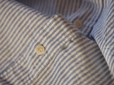 Close-up of a Sandro Oxford Shirt - Blue Stripe by Blue de Gênes. The textured, closely woven organic cotton pinstriped fabric with white corozo nut buttons is showcased, highlighting the pattern and texture.