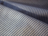 Close-up of Sandro Oxford Shirt by Blue de Gênes: features blue and white pinstripes on organic cotton, offering a textured look with thin vertical stripes on white. Slight gathers highlight its soft, flowing nature.