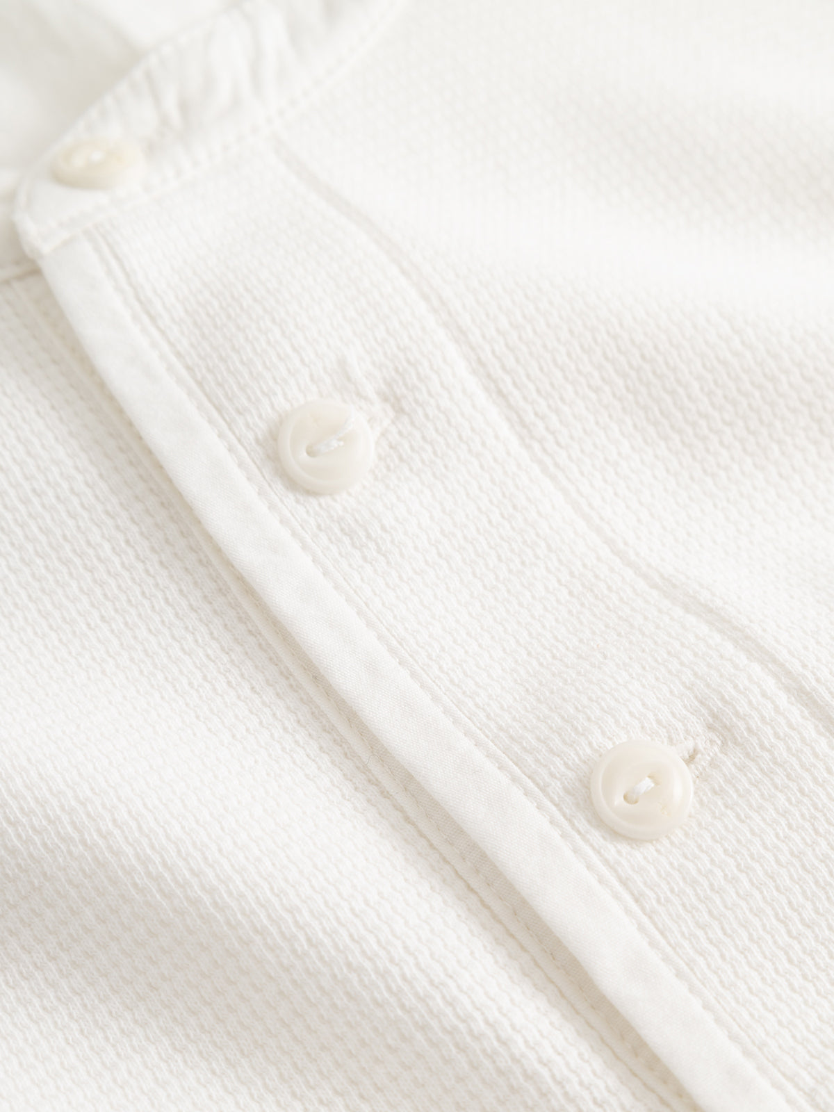 Close-up of the BGgreg L/S Grandad - White shirt by Blue de Gênes, crafted from white cotton poplin in a regular fit with three white corozo nut buttons and visible placket stitching.