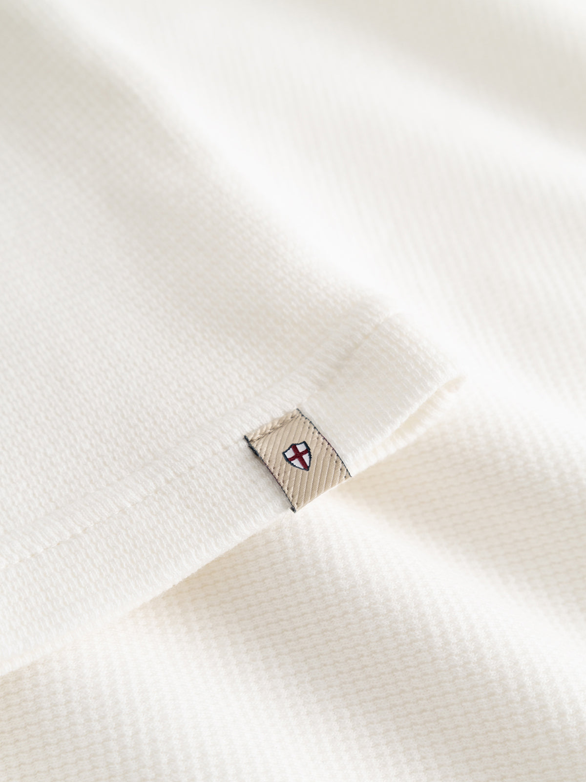 Close-up of the BGgreg L/S Grandad shirt in white by Blue de Gênes, crafted from soft, textured cotton poplin. A beige tag with a red and blue shield emblem is sewn into the seam.