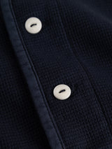 Close-up of the Blue de Gênes BGgreg L/S Grandad shirt in dark navy, featuring woven poplin fabric, a vertical seam, and two white corozo nut buttons.