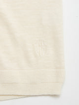 Close-up of the Blue de Gênes BGmonty Knit in Chalk, a cream-colored cotton-linen blend featuring a ribbed hem and an embroidered shield with a cross near the bottom edge.
