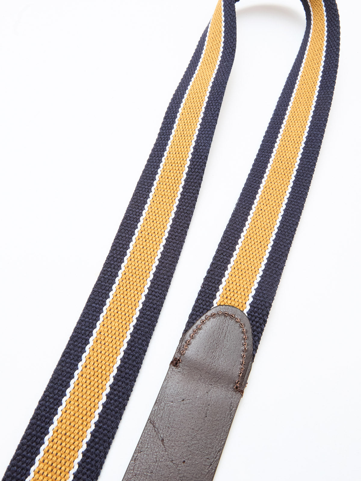 A close-up of the BGcollege Belt - Navy Stripe by Blue de Gênes, showing yellow, black, and white webbed stripes and a brown leather end with fine detailing against a white background.