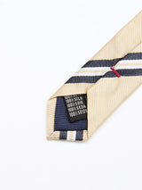 A close-up of the BGponsy Tie - Pale Khaki by Blue de Gênes, featuring beige and navy stripes, pointed end, and fabric label reading 100% silk in various languages on a white background.